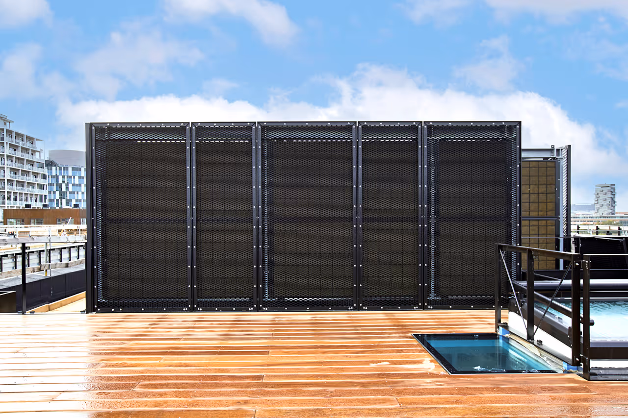 Black steel acoustic fence on a rooftop with wooden deck and blue sky background.