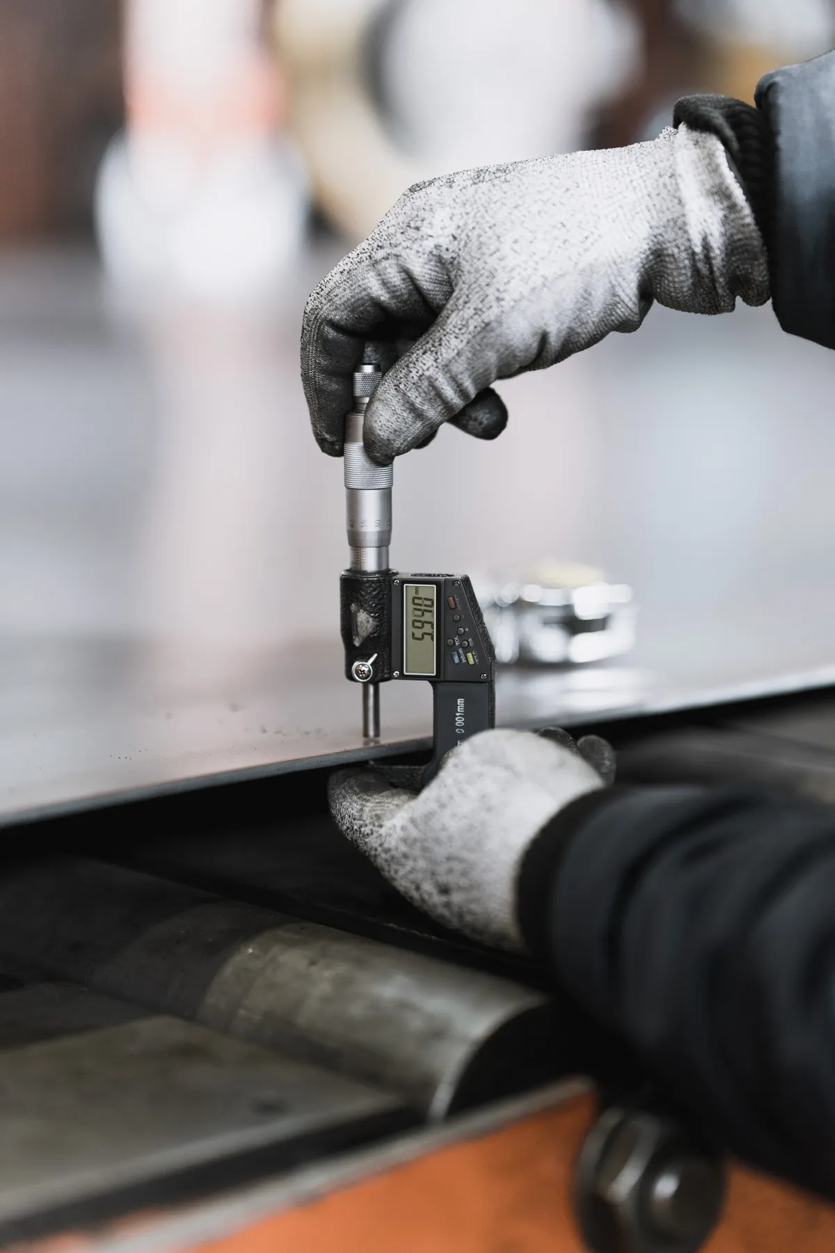 Mitarbeiter misst die Dicke eines Stahlblechs mit einem Mikrometer.