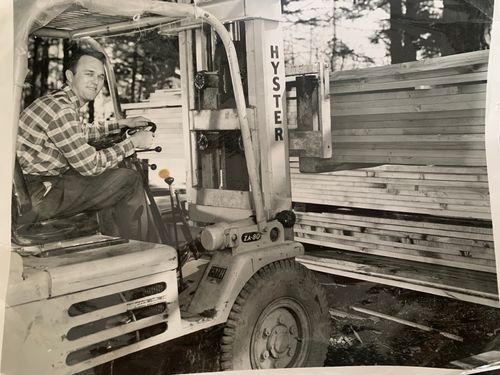 Man driving forklift carrying stack of lumber.