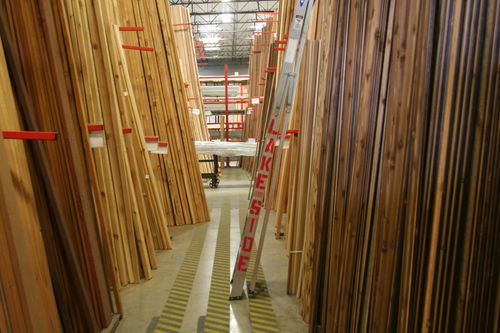 Stacked racks of lumber in a warehouse with a ladder.
