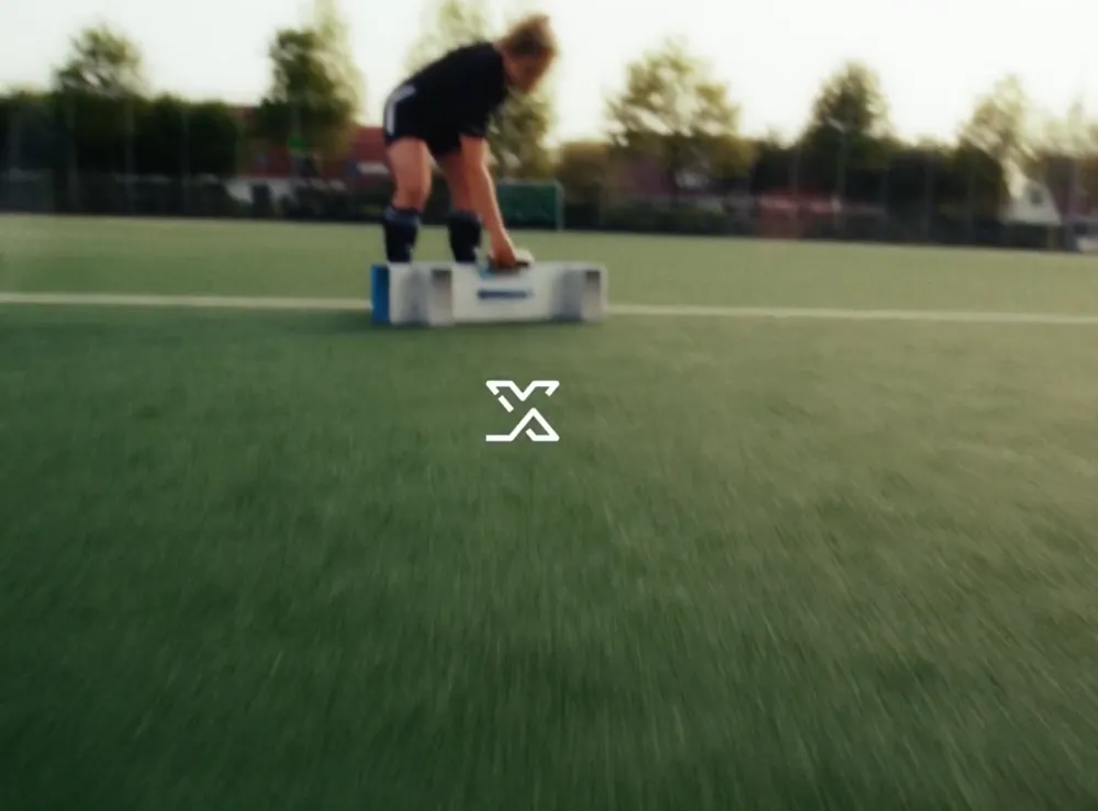 Sportieve vrouw plaatst een trainingsobject op een hockeyveld, met het X-Skills logo centraal in beeld.