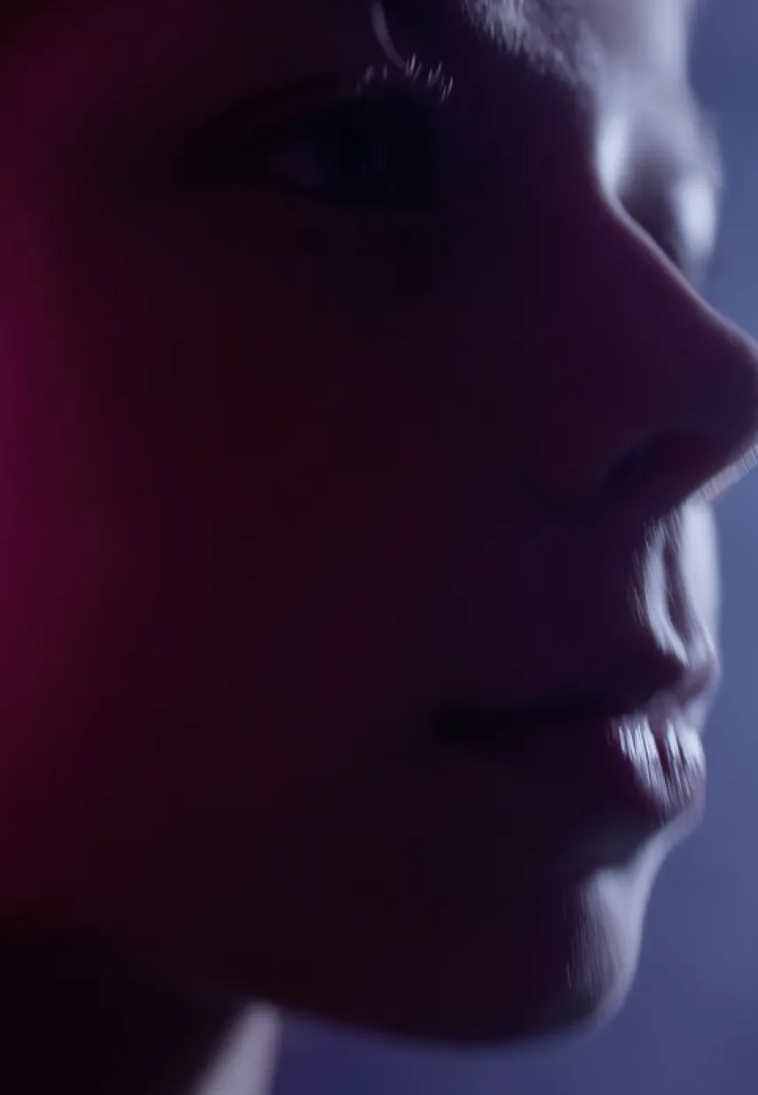 Close-up van het gezicht van een jong persoon in zacht paars en roze licht, met focus op het oog en de mond.