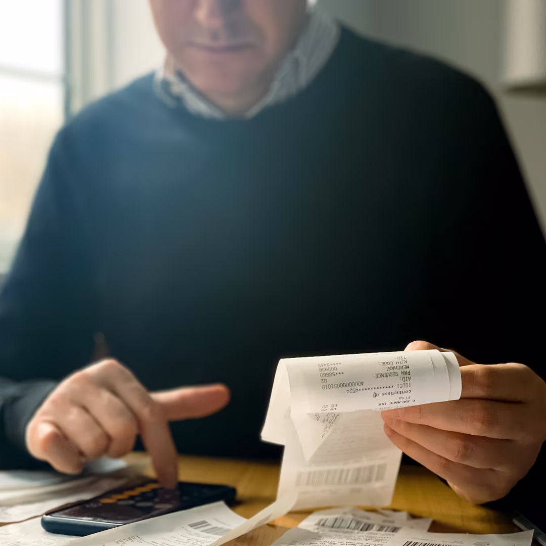 Person holding and reviewing receipts while using a calculator on a wooden table.