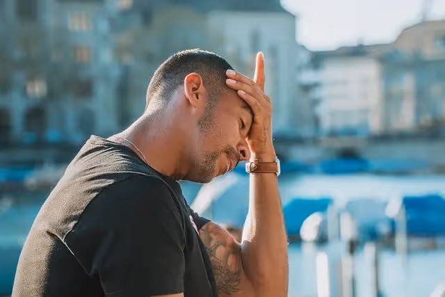 Man holding his head, looking stressed outdoors with blurred city background.