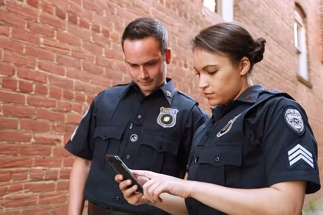 Two police officers standing in an alley reviewing information on a smartphone.
