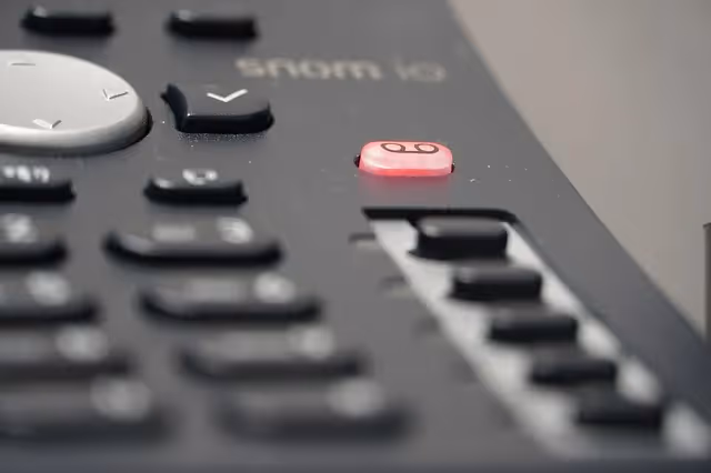 A close-up view of a VoIP desk phone keypad with the voicemail indicator button lit red.