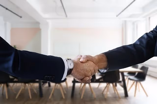 Close-up of two people in business attire shaking hands inside a modern office setting.