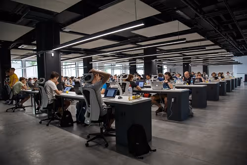 Large modern office space with rows of people working at desks on laptops.