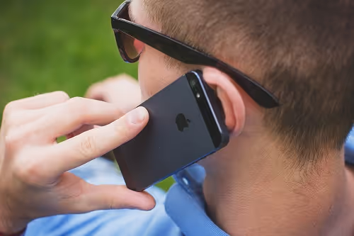 Close-up of a man holding an iPhone to his ear while talking outside.
