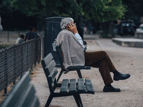 Older man sitting on a park bench and talking on his cellphone.