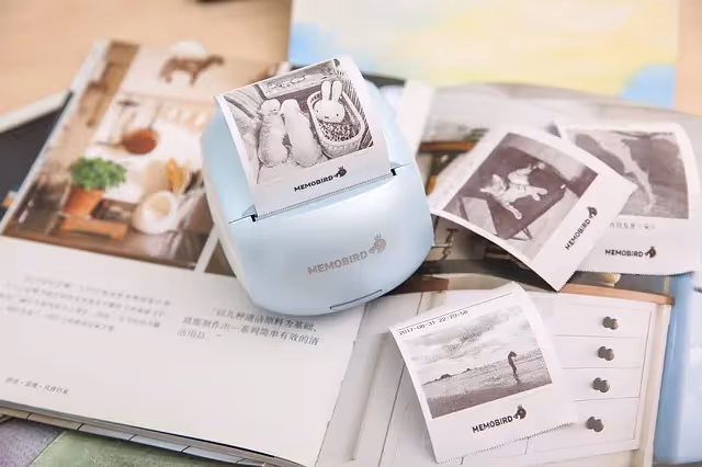 Small Memobird thermal printer on an open book, printing small photo slips that are spread around it.