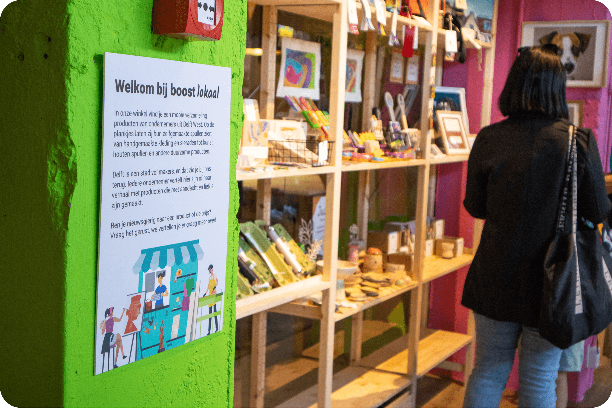 Foto van vrouw in Boost Lokaal met allemaal objecten in kasten. Daarnaast staat op een groene paal een welkom tekst.