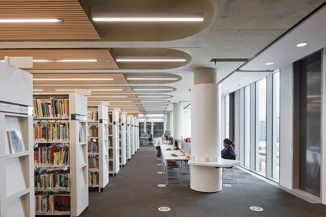 University library with architectural LED ceiling lighting — Class 2 low-voltage DC power for educational campuses. Photo: Unsplash, AI enhanced.