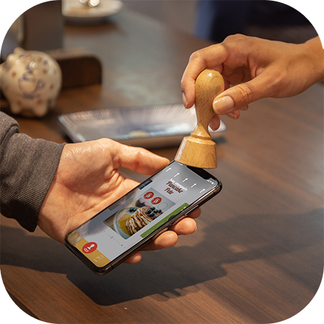 Stempelvorgang. Der NFC-Holzstempel wird zum stempeln an das Smartphone gehalten.