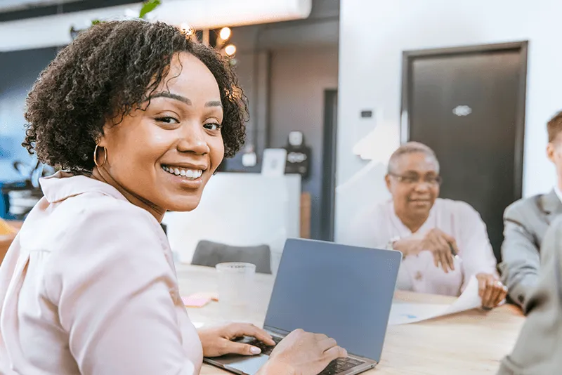 woman on legal team smiling over her shoulder in front of her laptop at a conference table