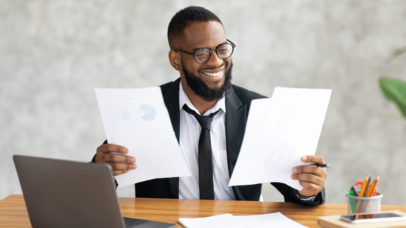 A man wearing glasses and a suit holds papers with some charts and statistics on them