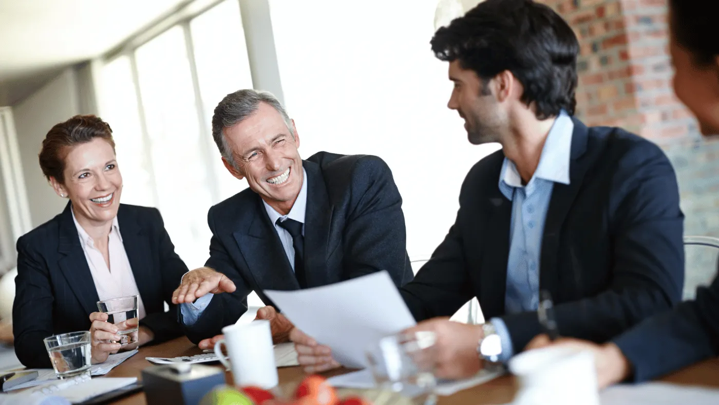 Three smiling attorneys wearing suits sit around a conference table with papers and glasses of water