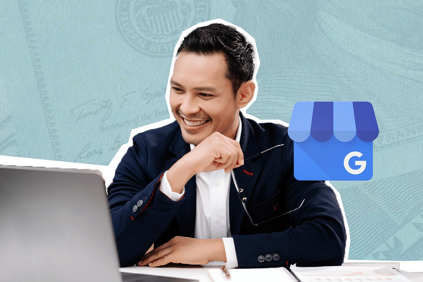Asian man wearing suit sits at desk and smiles at open laptop.