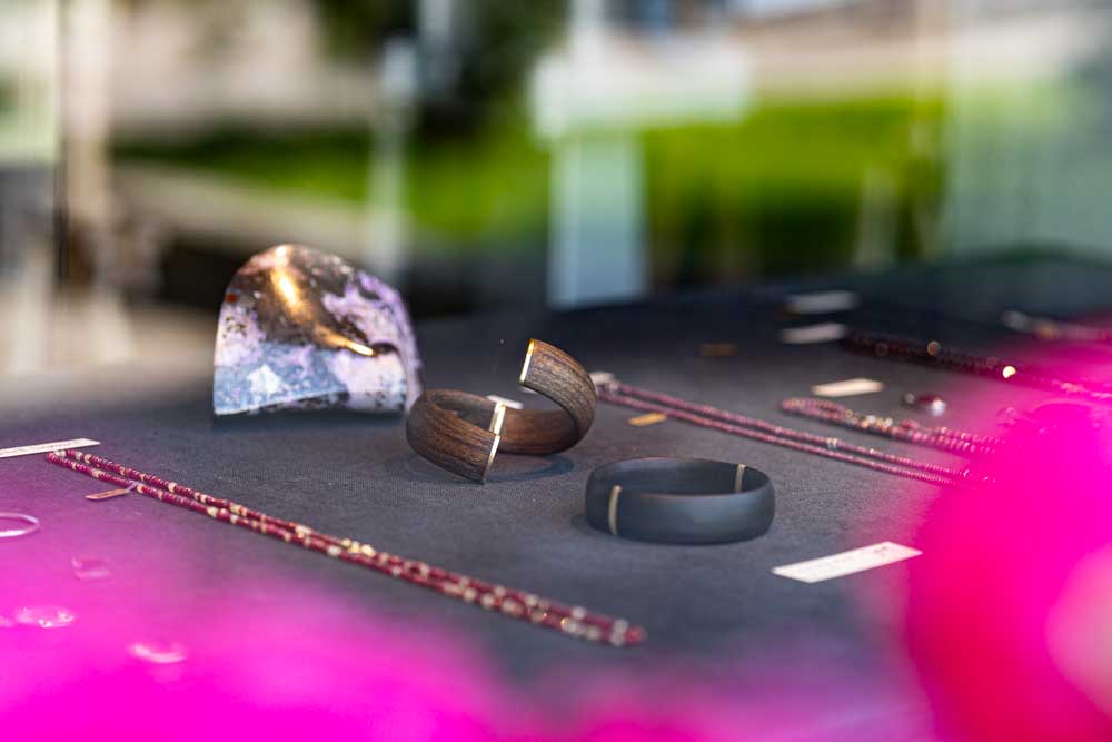 Display table with wooden bracelets and jewelry pieces on a dark surface with pink flower blur in the foreground.