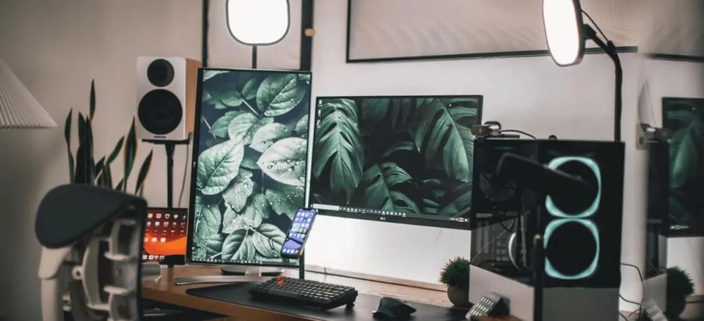 Escritorio con una computadora, monitor, teléfono, bocinas y micrófono.