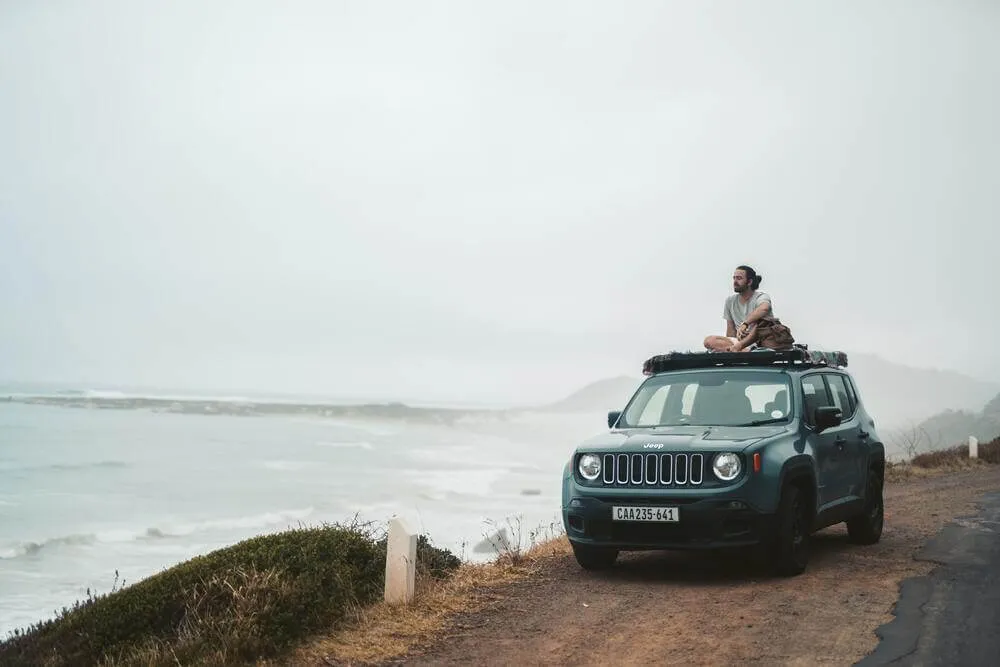 Turista arriba de un carro Jeep viendo la vista al mar