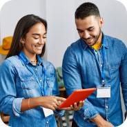 Two people wearing denim shirts smiling and looking at a red tablet together.