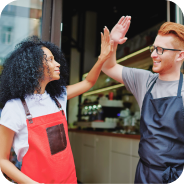 Two café workers smiling and giving each other a high-five inside a coffee shop.