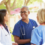 Three medical professionals, including a smiling male doctor with a stethoscope, engaged in conversation outdoors.