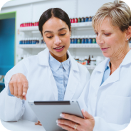 Two female scientists in lab coats discussing and reviewing information on a digital tablet in a laboratory.