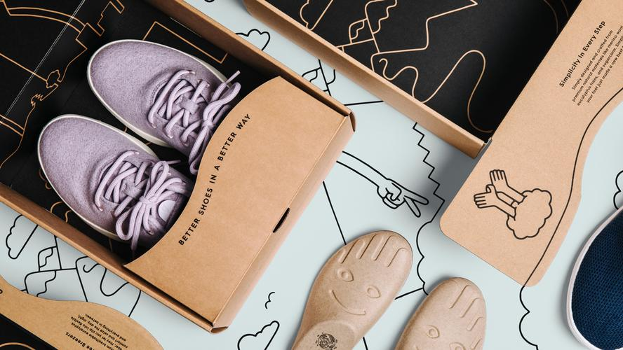 A pair of eco-friendly sneakers by Allbirds in lavender color displayed in a cardboard box that reads “Better Shoes in a Better Way.”