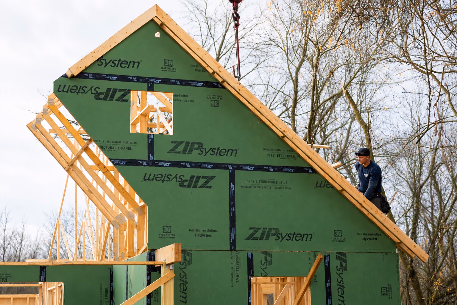 Construction worker installing green ZIP System sheathing on a wooden house frame roof.