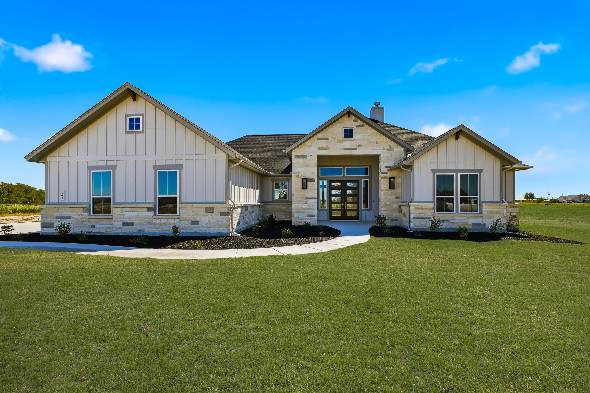 Exterior front view of a single-story Modern Hill Country ranch home with white stone masonry, dark trim, and a covered front porch.