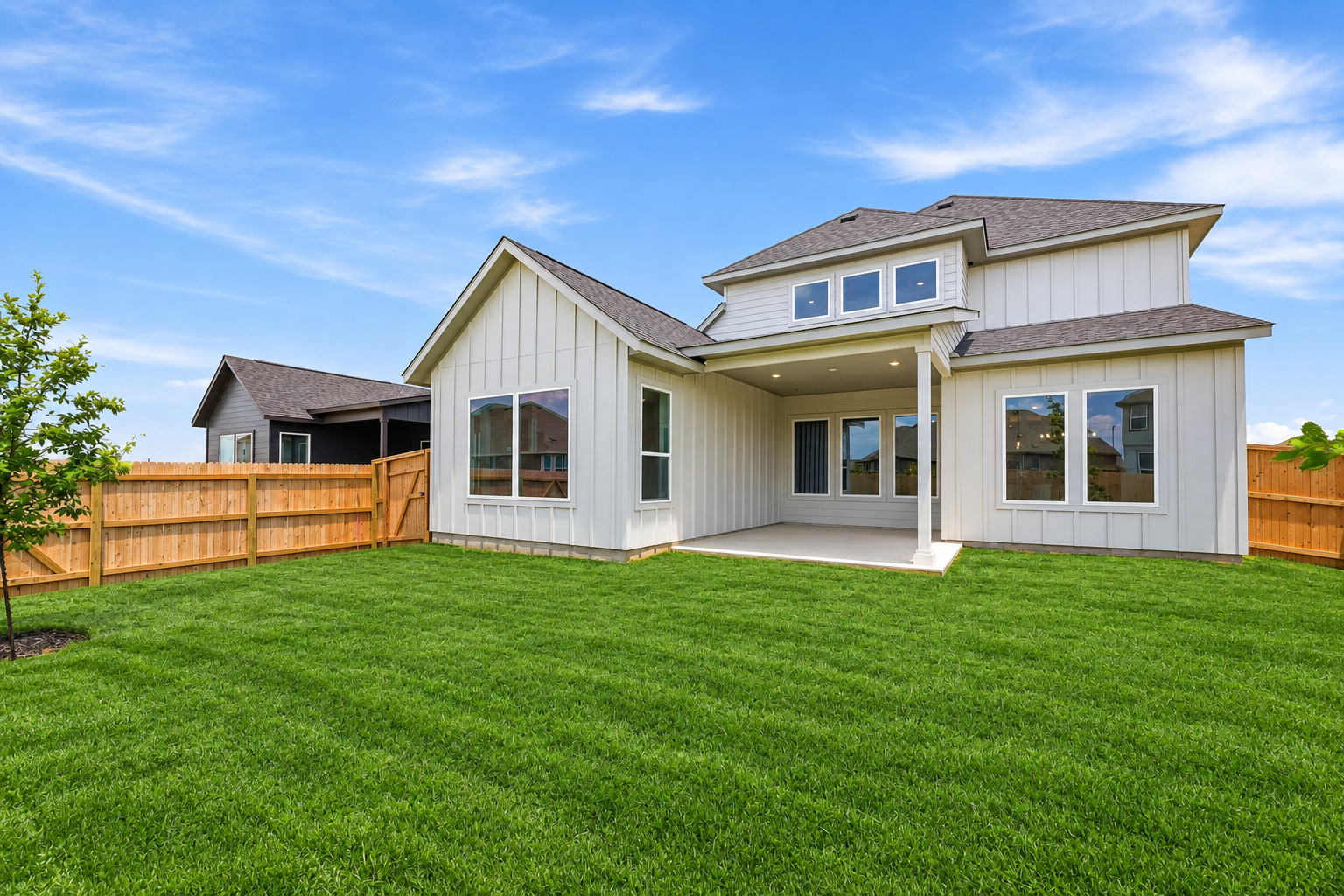 Rear exterior of The Travis home showing a covered back patio, spacious green backyard, and a full 6-foot cedar privacy fence.