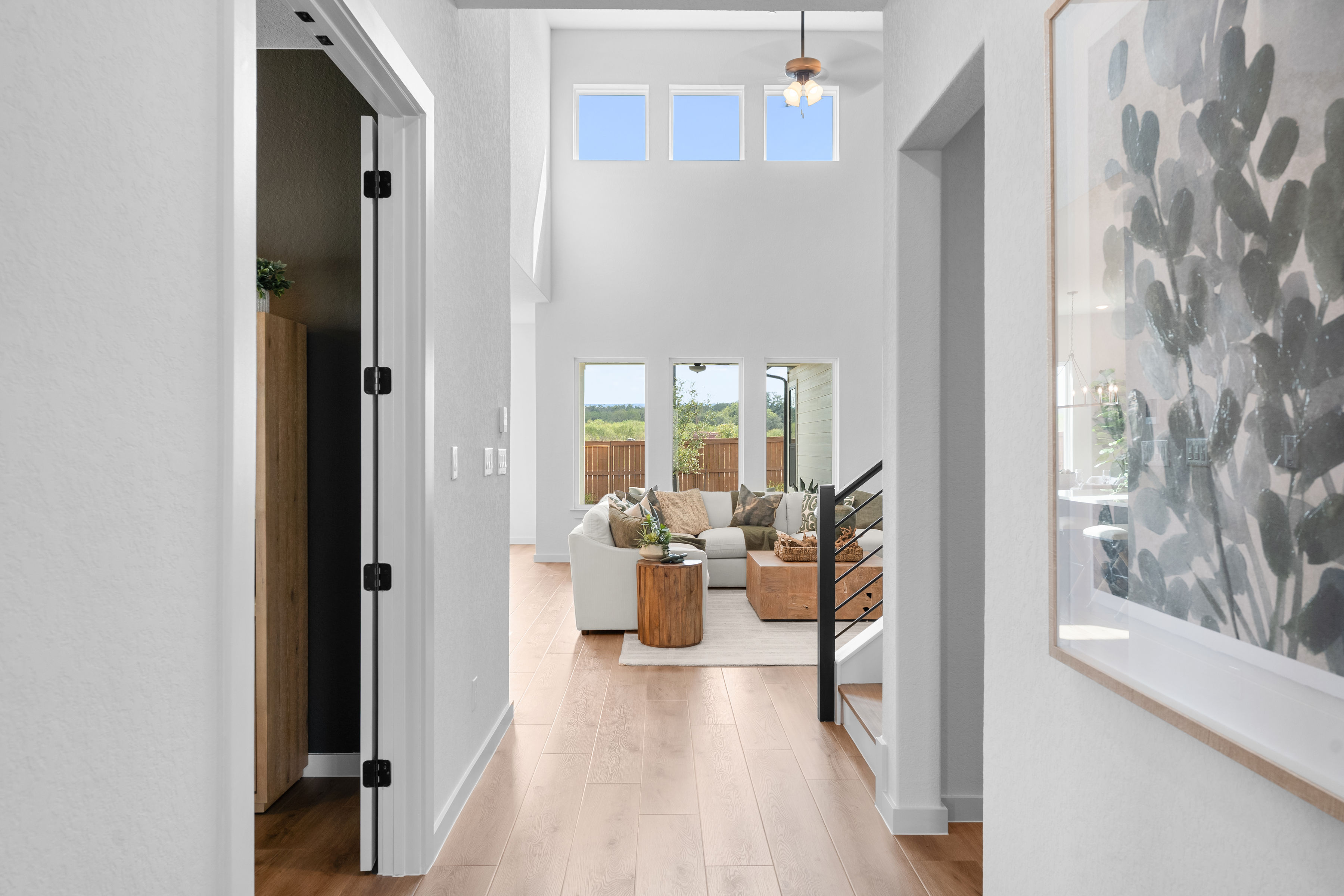 Modern Texas Hill Country entryway looking into an open-concept living room with high ceilings, large windows, light wood floors, and warm neutral decor built by Joseph Creek Homes in Greater San Antonio.