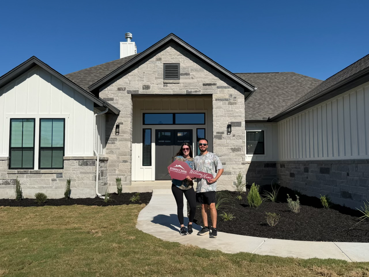 Happy new homeowners holding a Joseph Creek Homes key in front of their custom modern Hill Country home with stone masonry in Greater San Antonio.