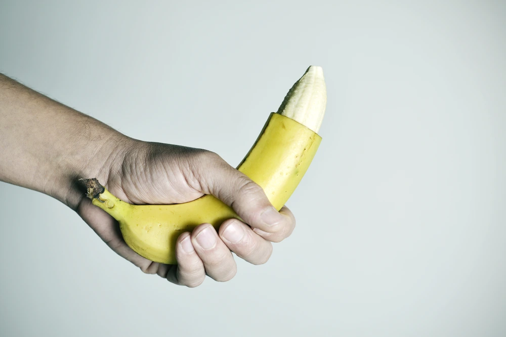 Symbolbild beschnittener Penis: Hand hält Banane mit entfernter Schale an der Spitze. | GoSpring
