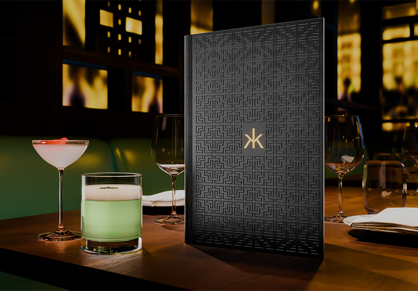 Bespoke cocktail menu designed by Knockout for Hakkasan, displayed beside cocktails, with a black lattice-patterned cover echoing the restaurant’s wooden screens and a gold Hakkasan logo.
