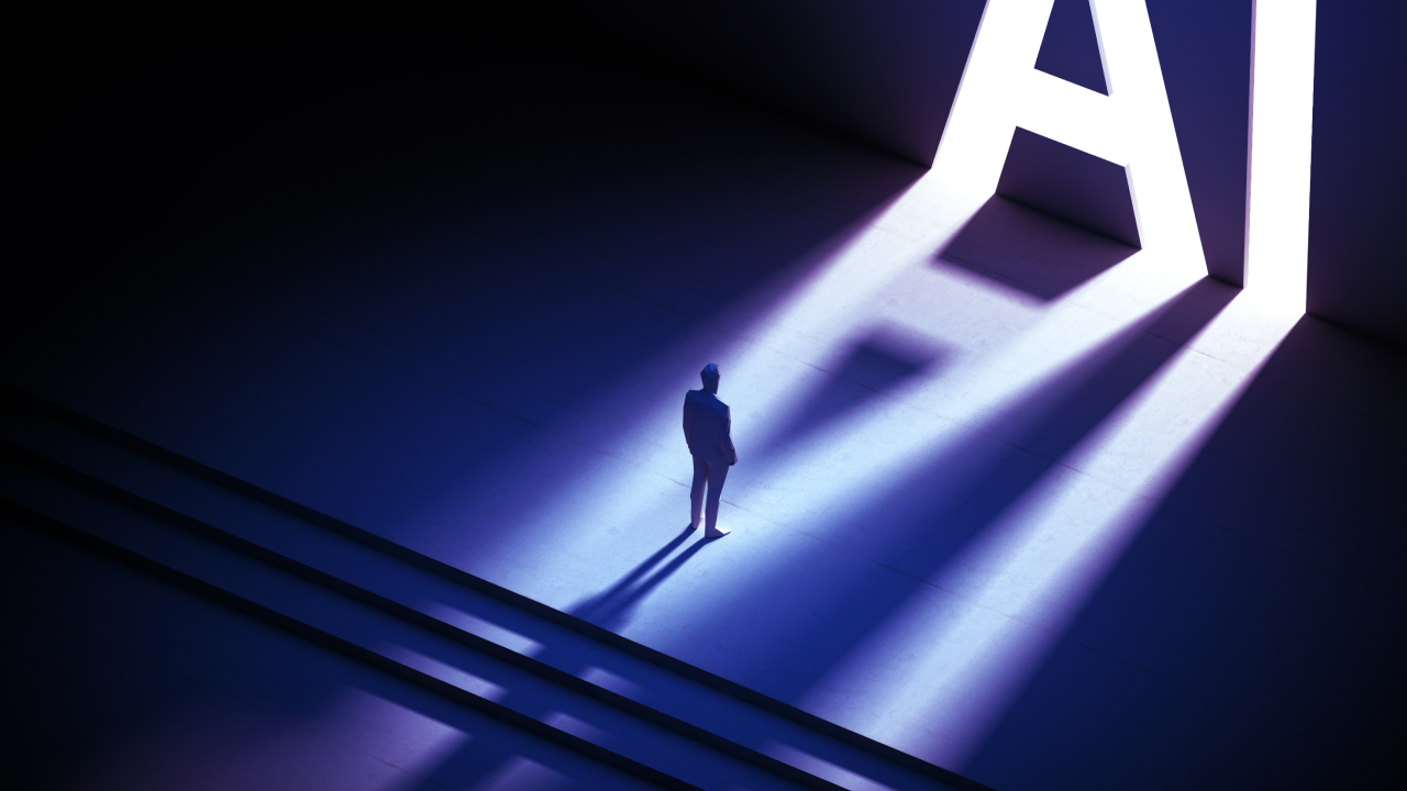 A lone figure stands in front of a towering, glowing “AI” symbol, with dramatic shadows cast across the floor, representing the scale and impact of artificial intelligence on the future of work and technology.