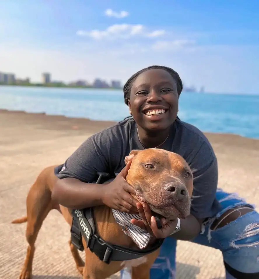 TikToker Riziki Ilenre smiling while holding her dog by a body of water.