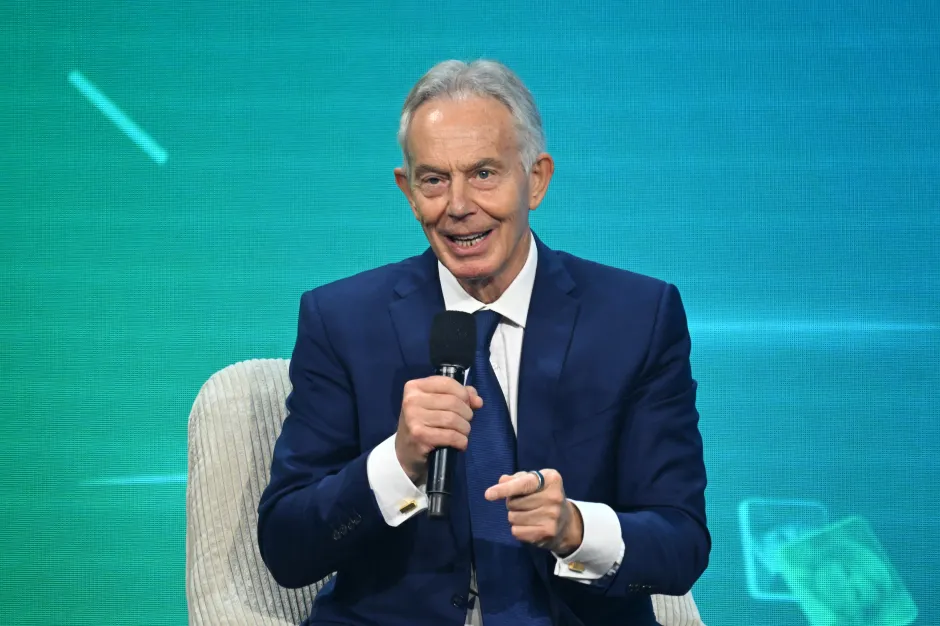 Tony Blair in a blue suit holding a microphone and gesturing.