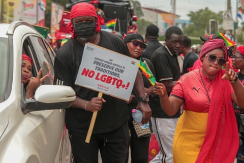 People carrying placards reading 'Preserve our traditions, No LGBTQ+!' and Ghanaian flags march in a street alongside cars