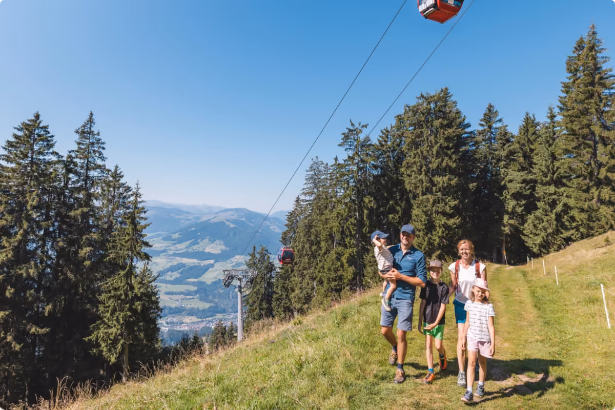 Familie mit drei Kindern beim Wandern unter der Gondelbahn in Hopfgarten an der Hohen Salve in Tirol im Sommer.