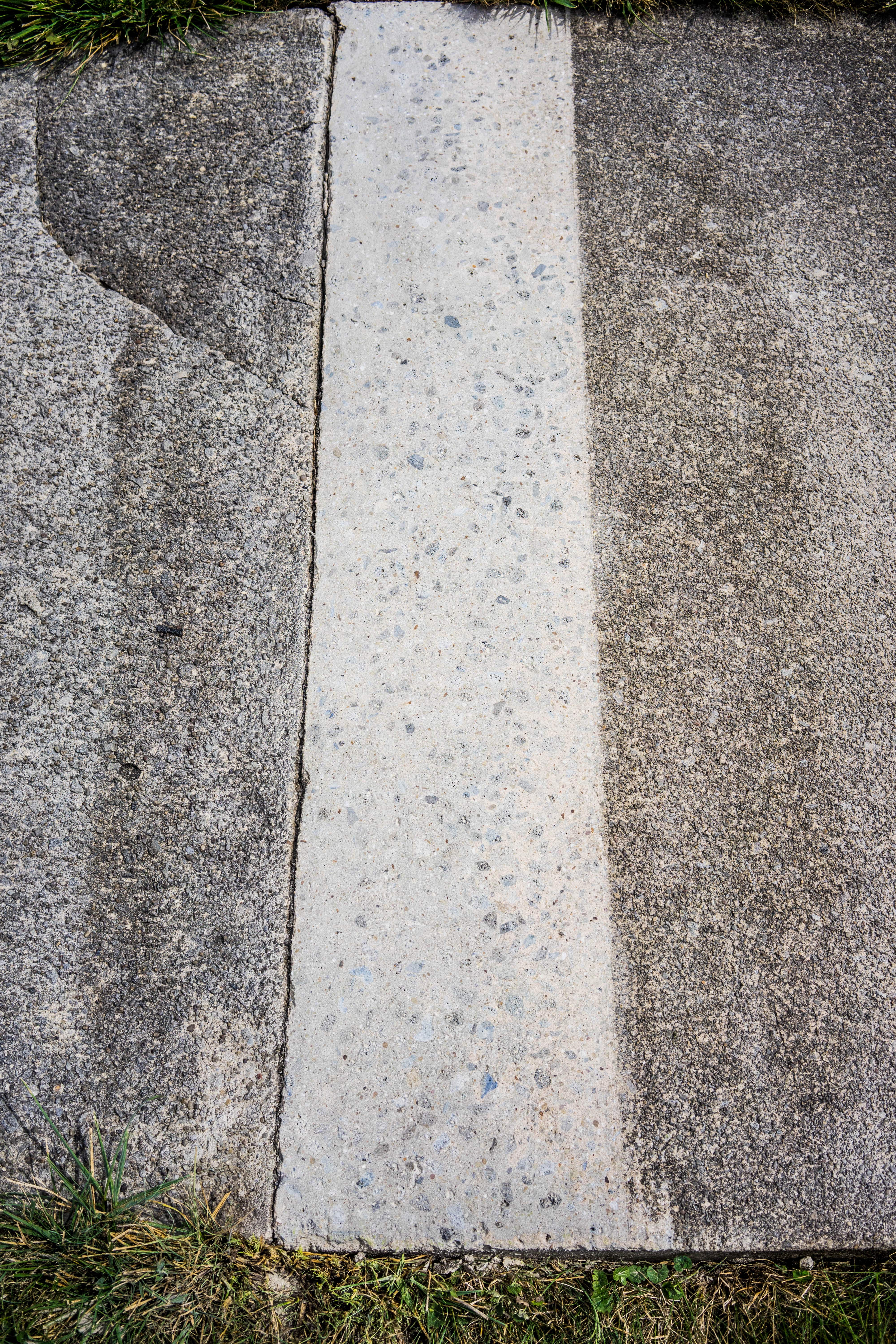 Sidewalk pad with the trip hazard ground down to be level with the adjacent pad. The ground part is lighter in color from the abrasion.
