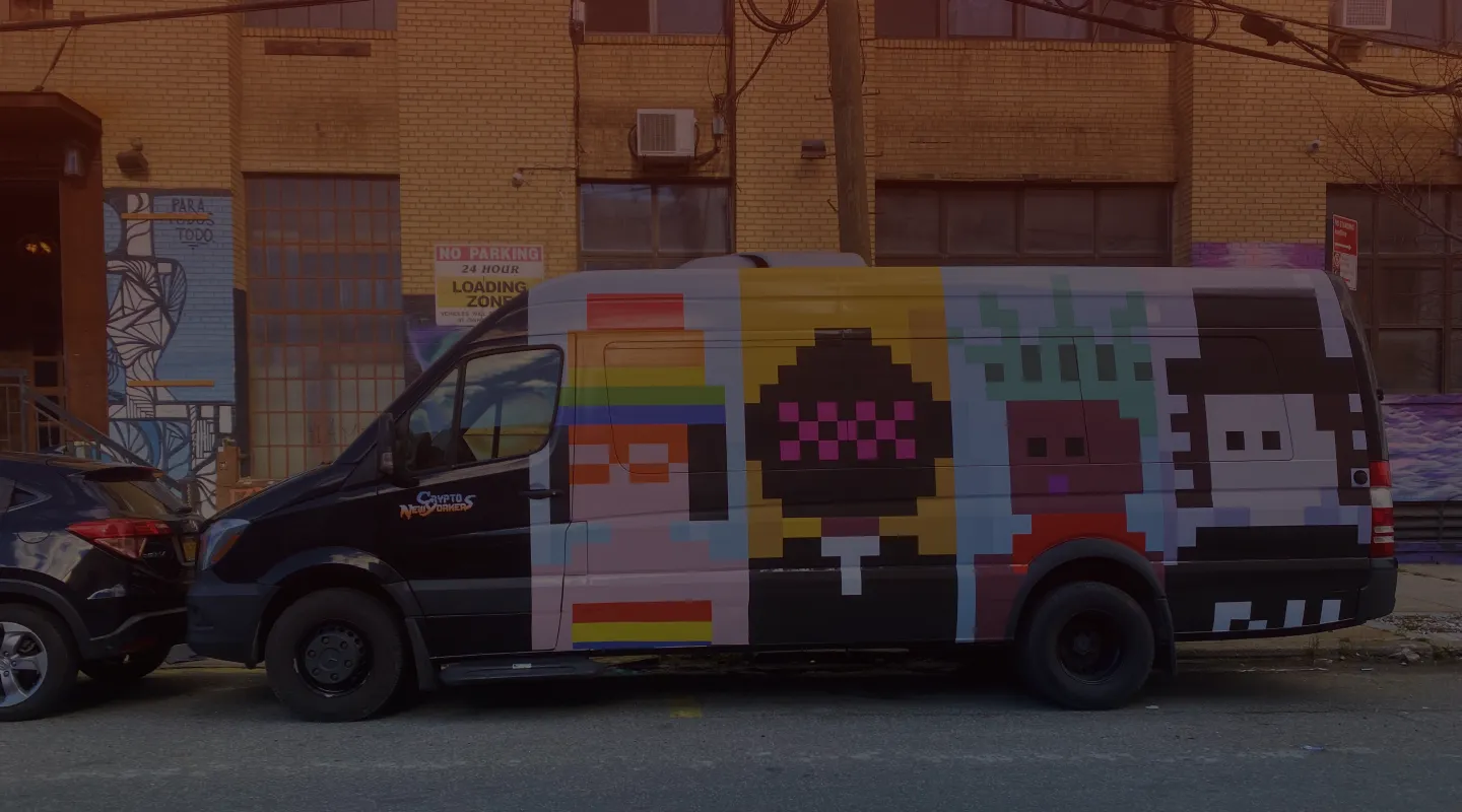 Black van parked on a city street with pixel art characters in vibrant colors painted on its side, including a figure with glasses and rainbow headband, a dark figure with pink decorations on a yellow background, a character with green spiky hair, and a white face with black hair, near a brick building with graffiti and signage.
