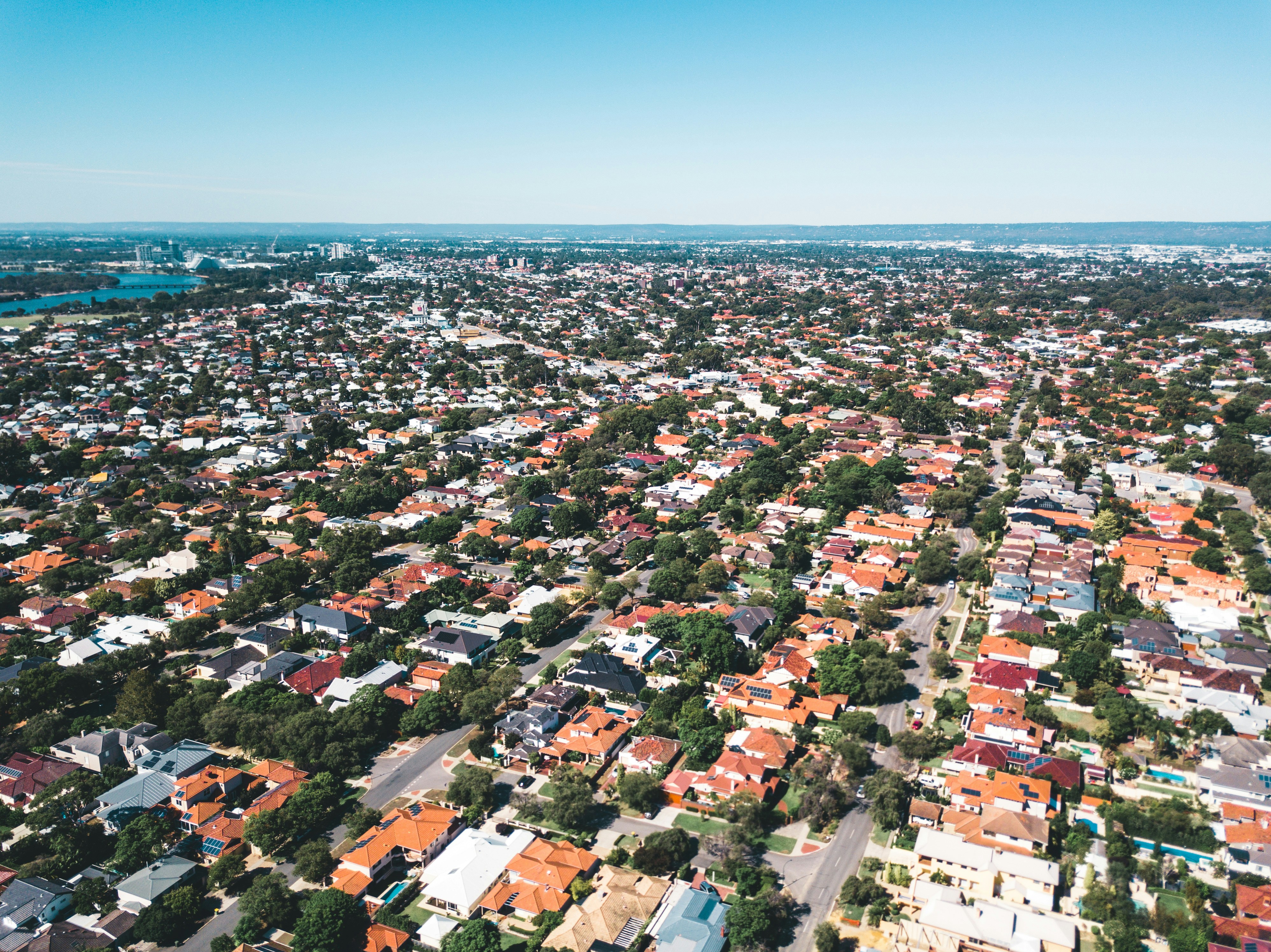 Aerial view of a suburban neighborhood with houses, tree-lined streets, and a clear blue sky.
