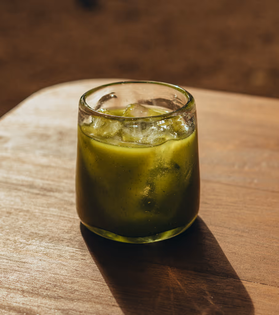 Glass with a green iced drink on a wooden surface casting a shadow.