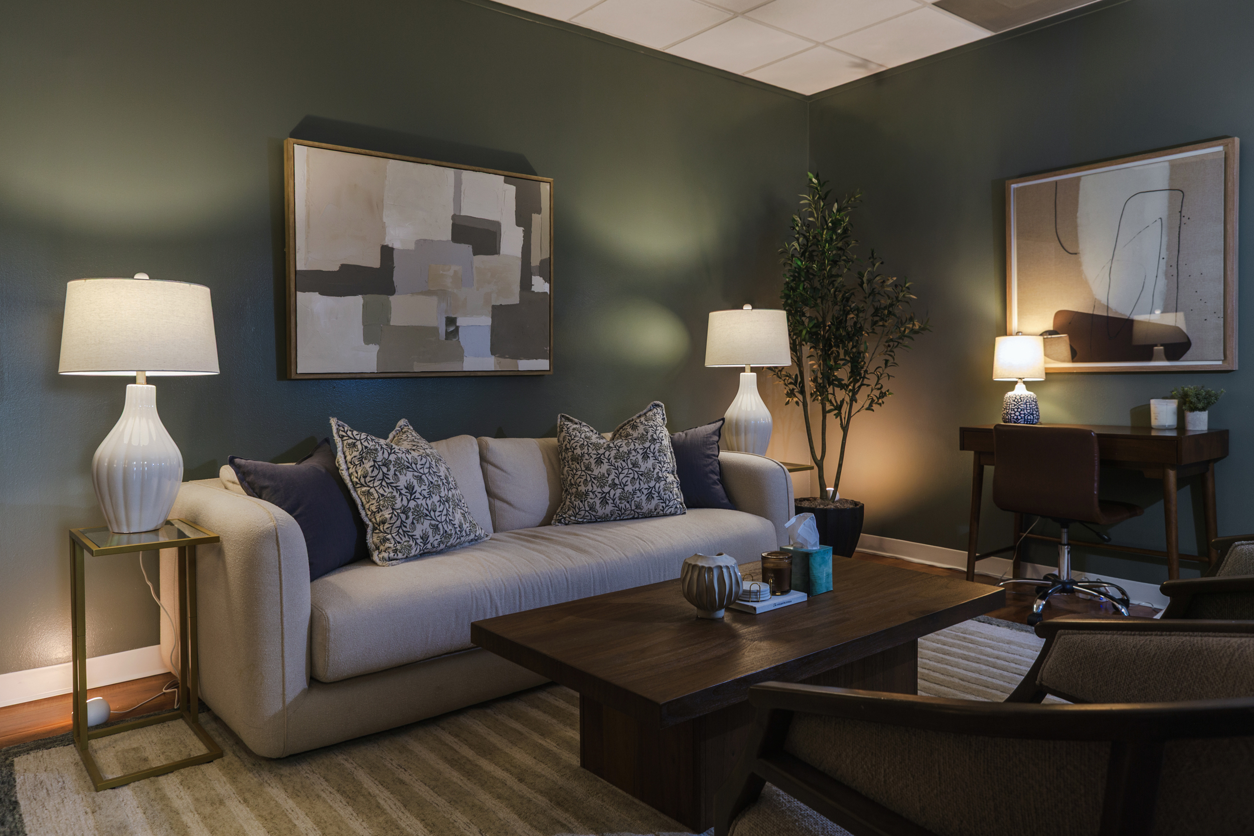 Therapy office at Decades Counseling with a beige sofa, coffee table, and forest green walls