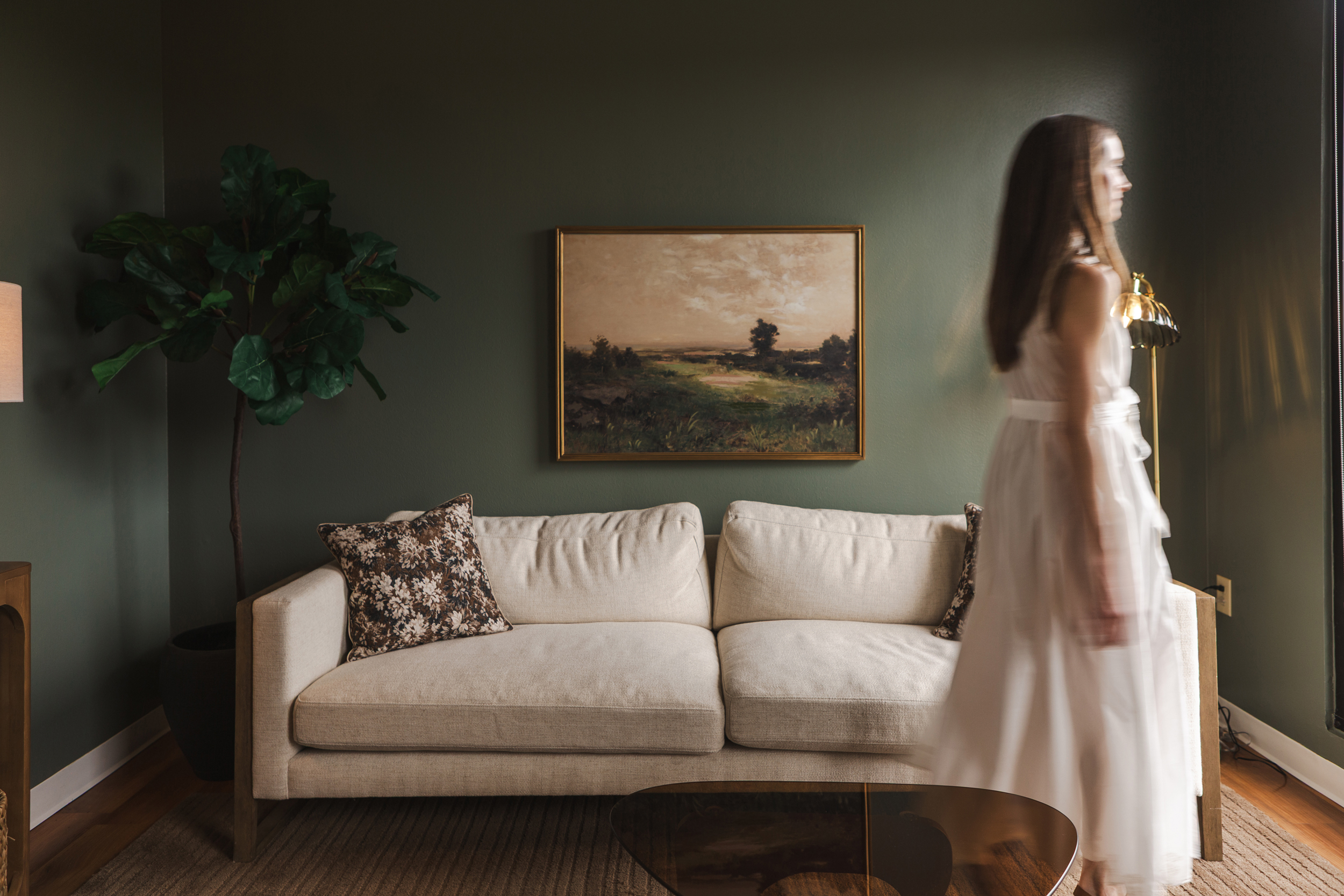 Therapy room with cream sofa, olive green walls, framed landscape painting, and leafy indoor plant