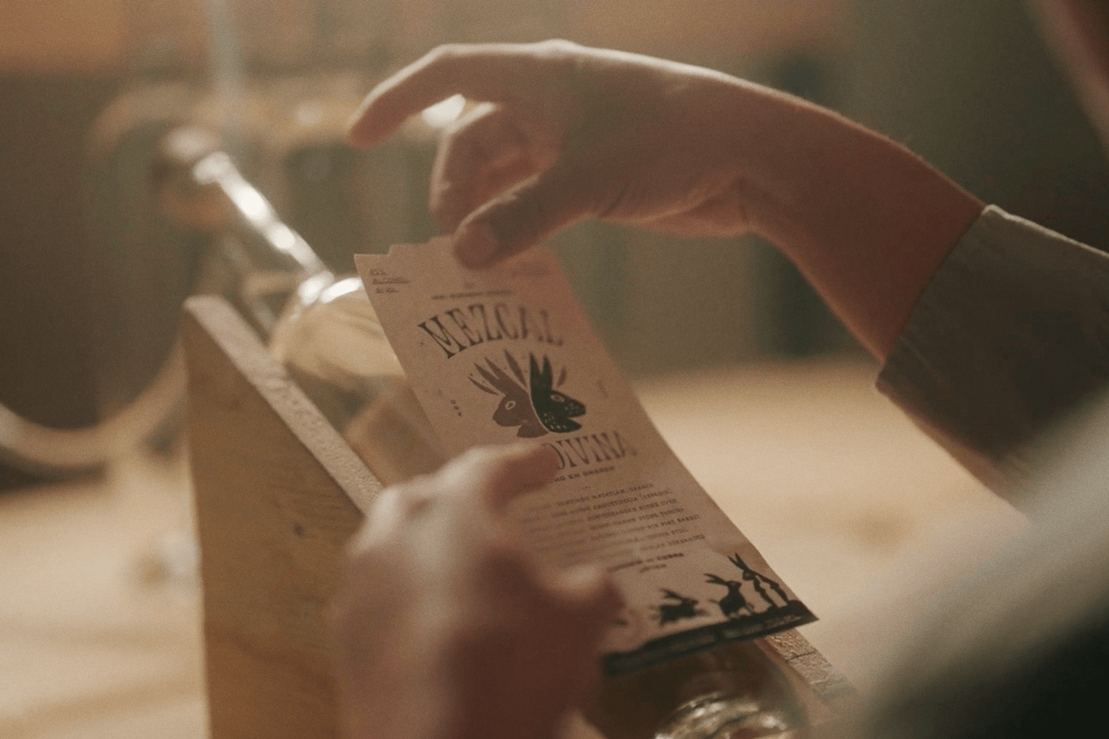 Hands applying the front-label to a bottle of Sal Divina Mezcal.