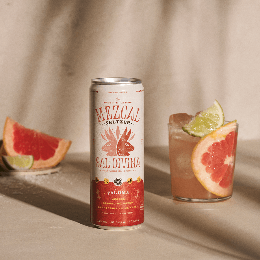 A photograph of Sal Divina's Paloma seltzer with a Paloma cocktail in an elegant glass to the side, featuring a grapefruit slice and a lime slice.
